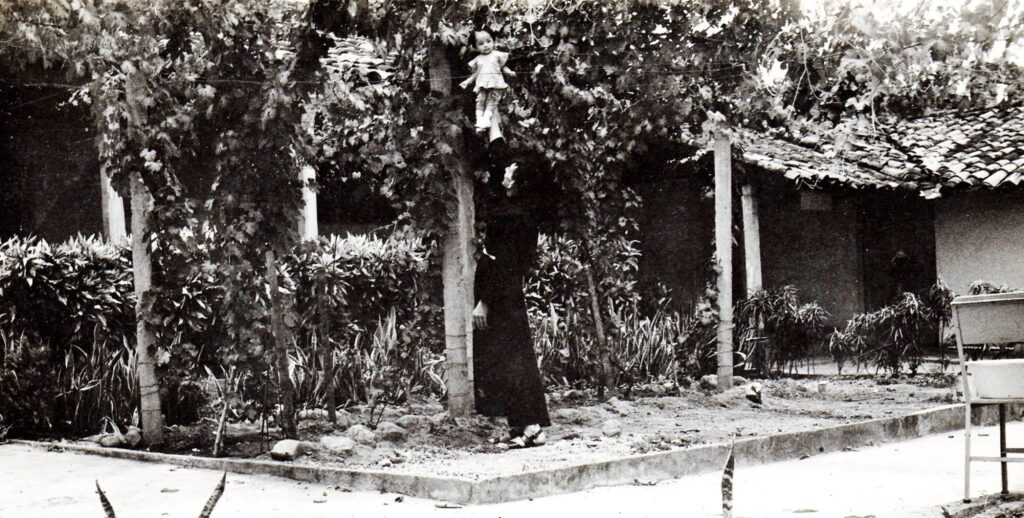 Cosme Spessotto alzando a una niña a los gajos de uvas, en el viñedo del convento parroquial de San Juan Nonualco, en 1975